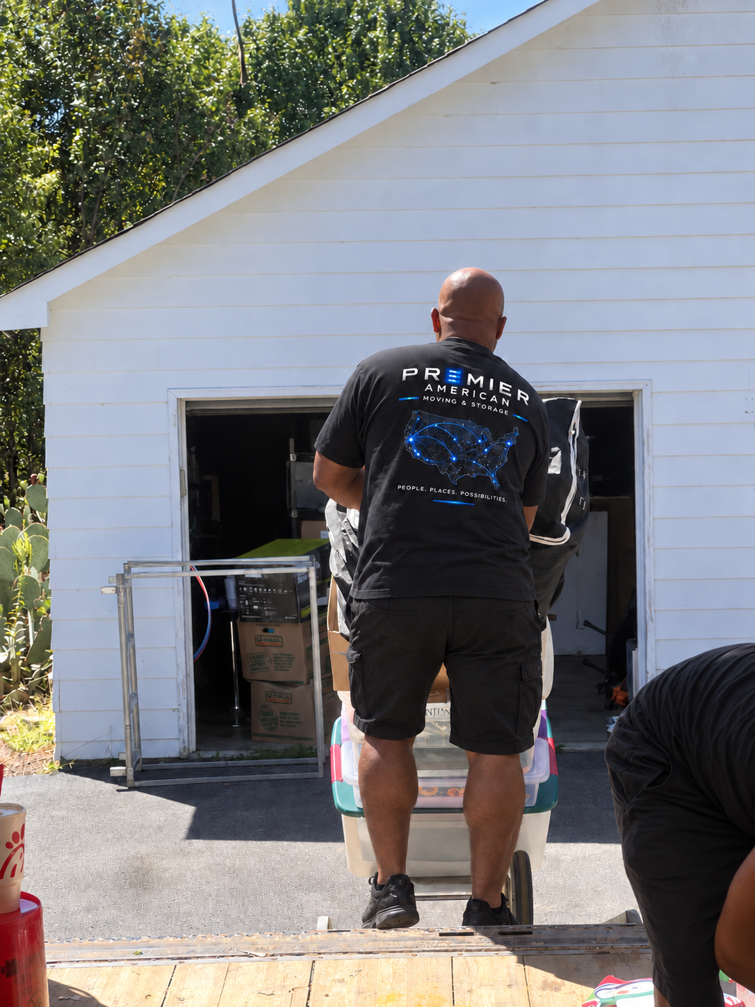 Premier mover in a black uniform, black shorts and black sneakers working outside a garage, with another crew member beside him